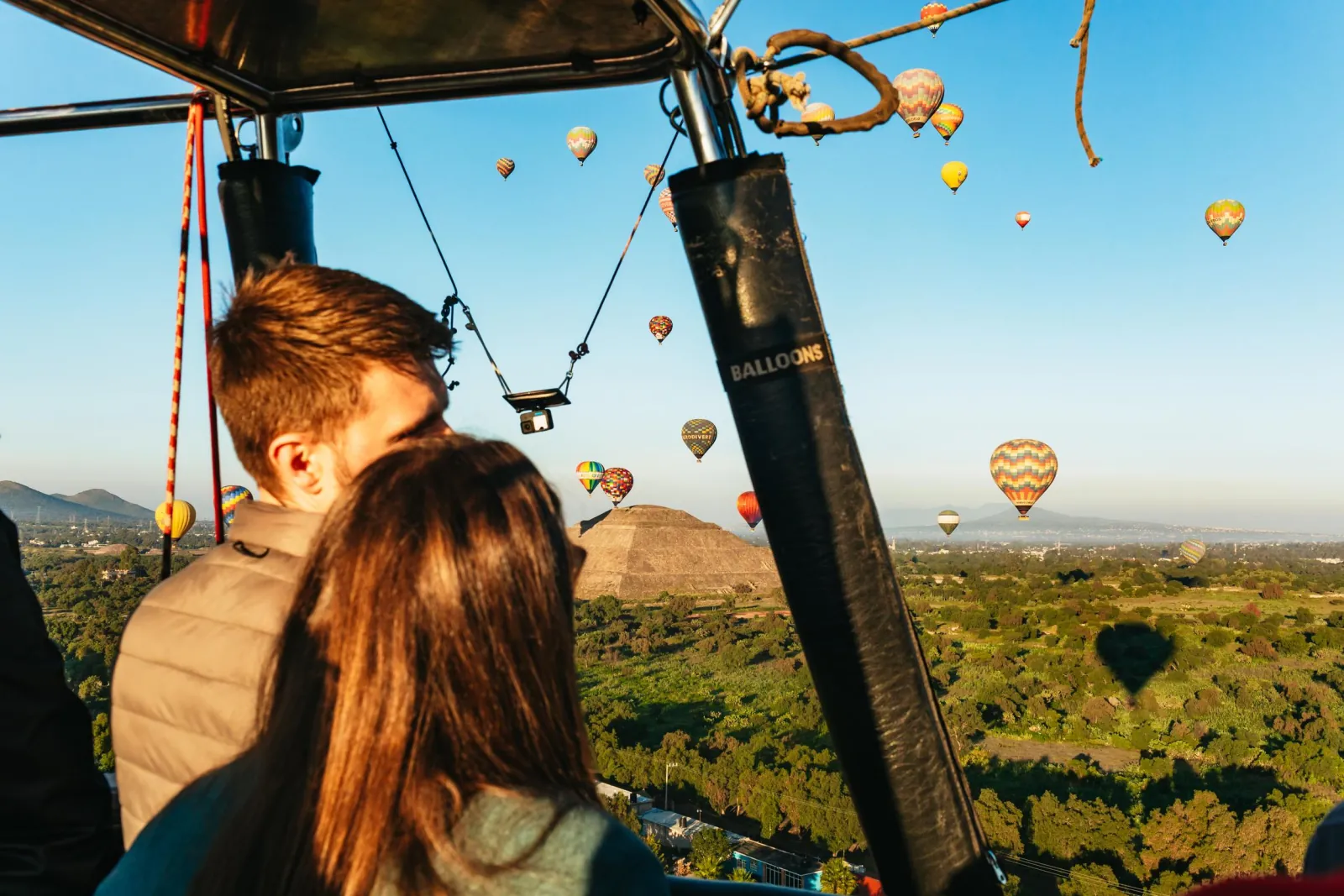 Two passengers in the basket looking toward a pyramid with balloons all around