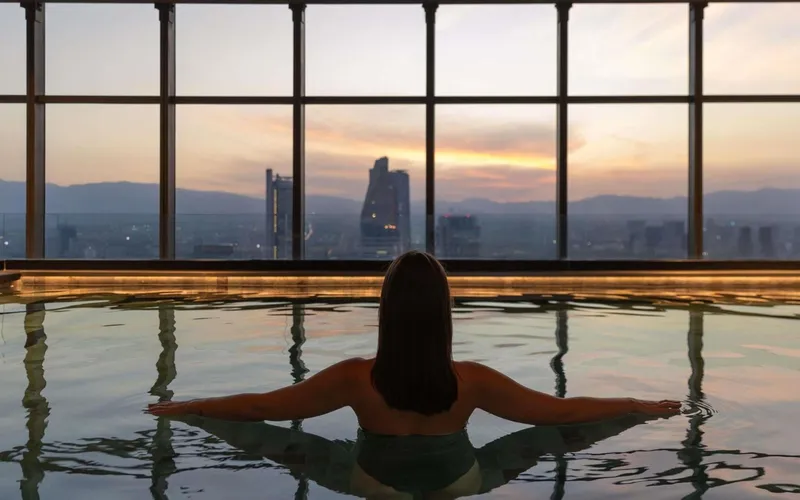 Guest in the glass-walled indoor pool at Sofitel Mexico City Reforma, looking over the city at dusk