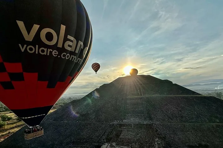 The sun rising over a pyramid with a black and red balloon in the foreground