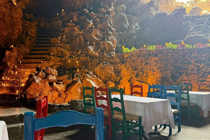 Candlelit cave steps and rock wall above tables set with colorful chairs