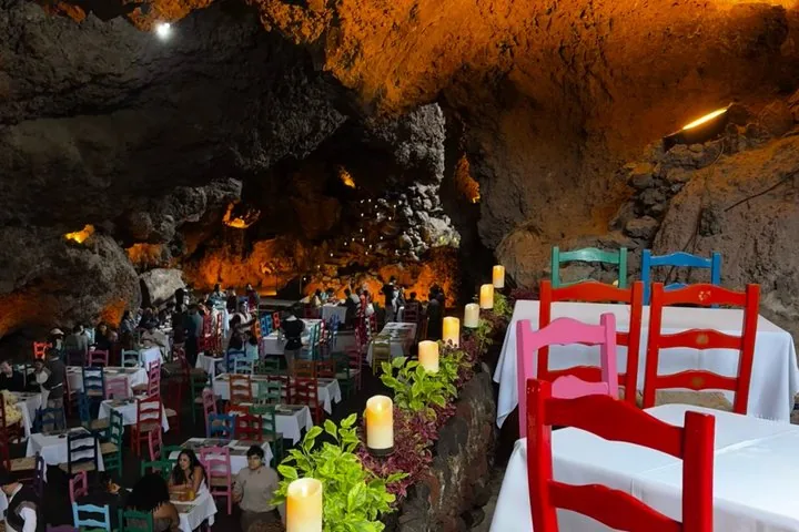 A busy cave restaurant with colorful chairs, candles and an orange glowing ceiling