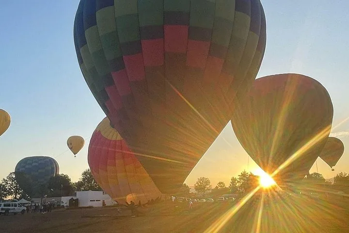 Balloons inflating on the field at sunrise with the low sun flaring between them