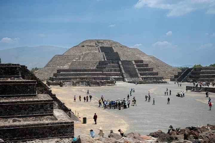 Stepped pyramid at the end of a wide plaza with small groups of visitors