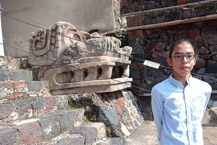 Teenager with glasses standing beside a carved stone serpent head on a temple platform