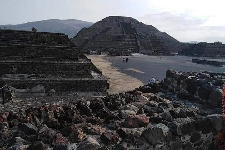 Stepped pyramid seen across a stone plaza at Teotihuacán with a dark rock wall in front