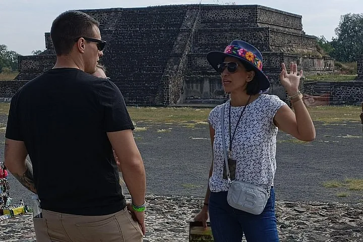 Guide in a blue hat talking to a visitor in front of a stone platform