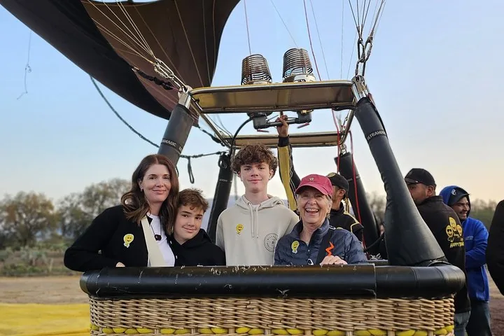 Four passengers smiling in a wicker basket at the launch field before takeoff