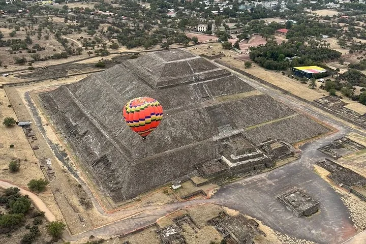 Aerial view of a balloon floating over a large stepped pyramid and surrounding ruins