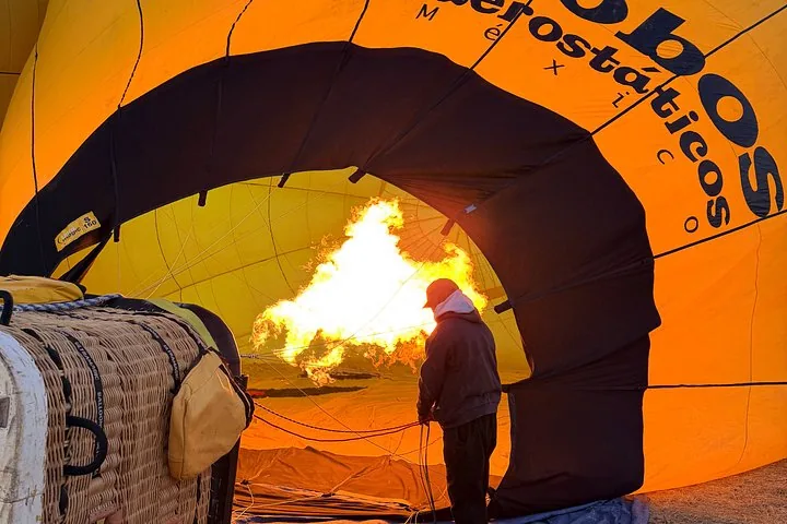 Crew member standing inside an orange balloon envelope as the burner flame inflates it