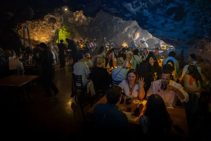 Guests seated at long tables inside a dimly lit natural cave restaurant