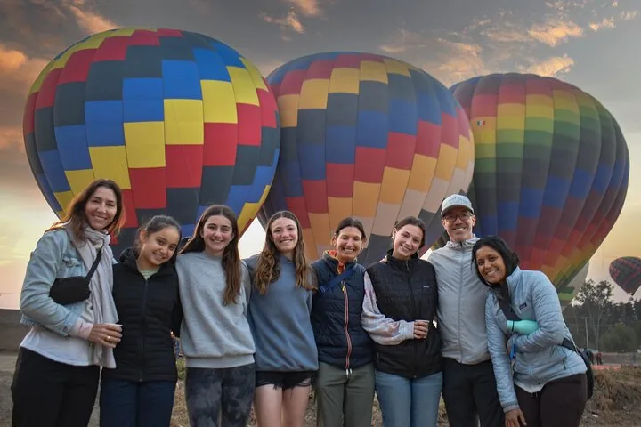 Eight guests posing in cold-weather jackets in front of three inflated balloons at dawn