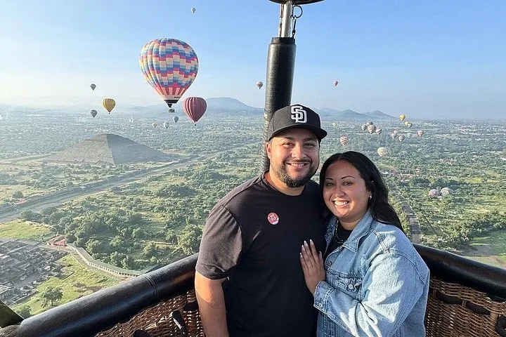 A couple in a basket with the Pyramid of the Sun and balloons behind them