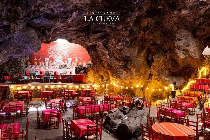 Tables and string lights inside a cave restaurant with a lit sign reading La Cueva