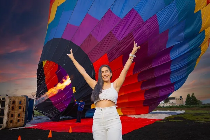 A woman with raised arms in front of a balloon being inflated with burner flame