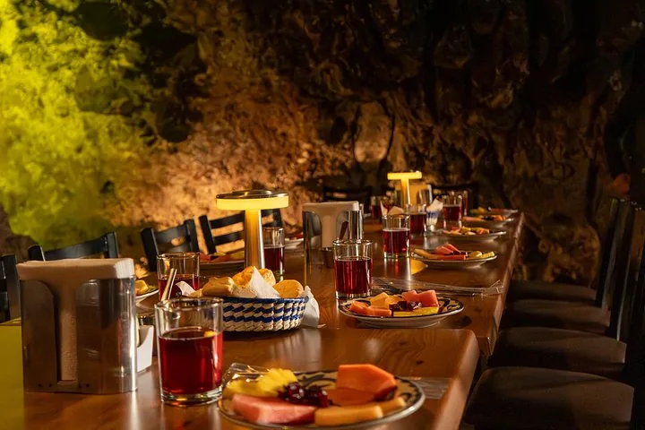 Long breakfast table set with fruit plates and tea glasses inside a cave