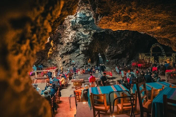 Diners at tables with striped cloths inside a lit natural cave restaurant
