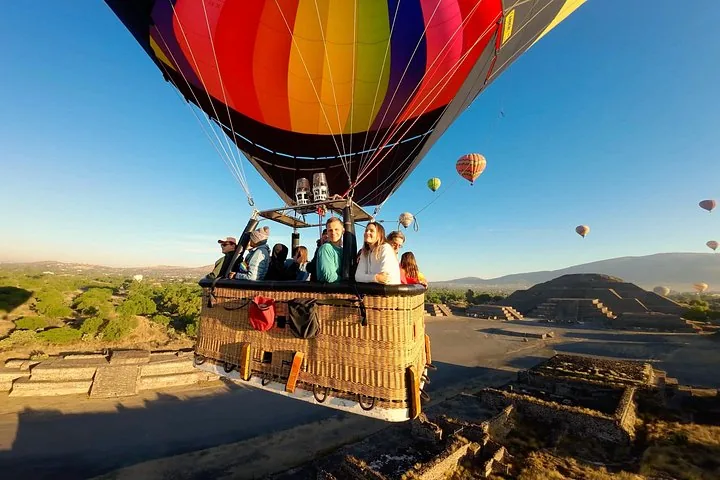 Passengers in a wicker basket under a rainbow balloon with a pyramid and valley below