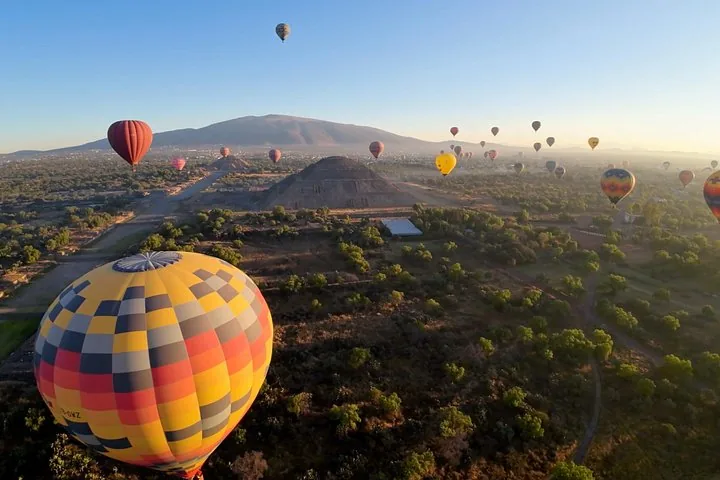 Colorful balloons floating over the Teotihuacán valley with a large pyramid and a distant mountain