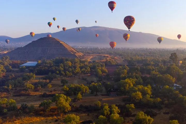 Balloons rising at sunrise over the Pyramid of the Sun with mountains behind
