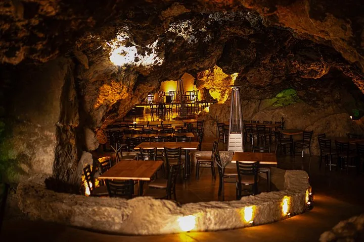 Tables and chairs inside a warmly lit natural cave restaurant