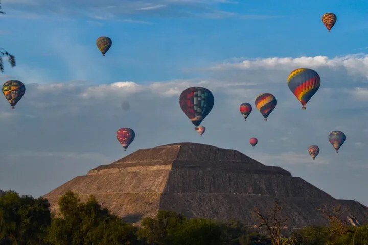 Balloons in the sky above a stepped pyramid under scattered cloud