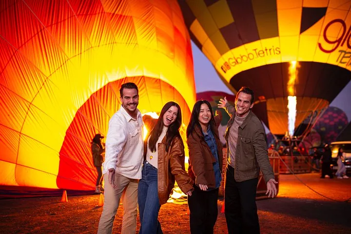 Four guests posing in front of a glowing balloon inflating with burner flame